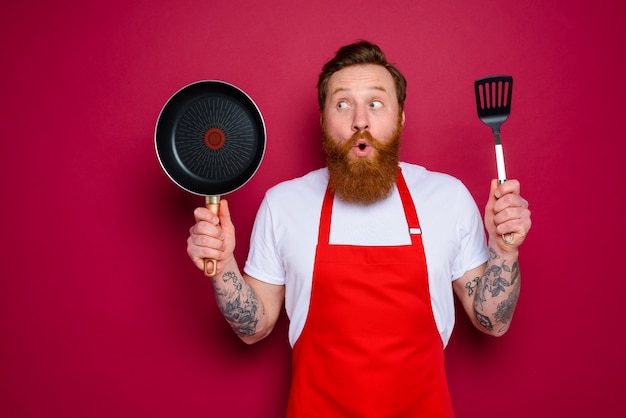 Surprised chef with beard and red apron is ready to cook