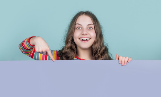 Surprised child behind blank blue paper with copy space for advertisement