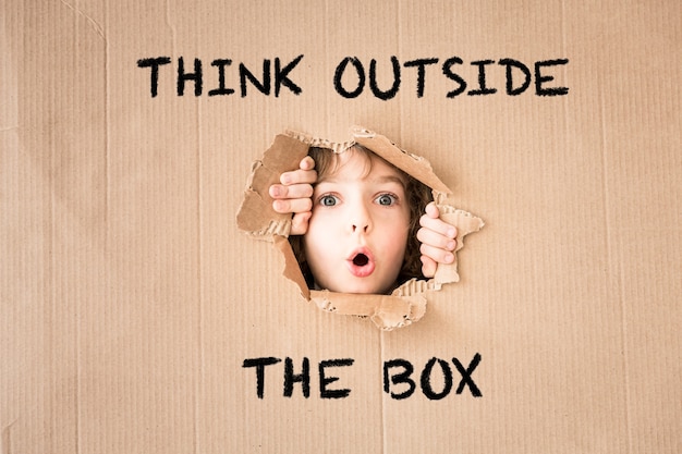 Surprised child looking through hole of cardboard. "Think outside the box" text