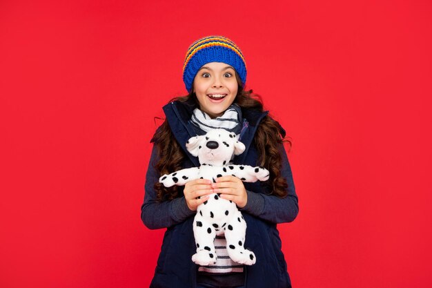 surprised child in puffer jacket hold toy teen girl on red background happy childhood