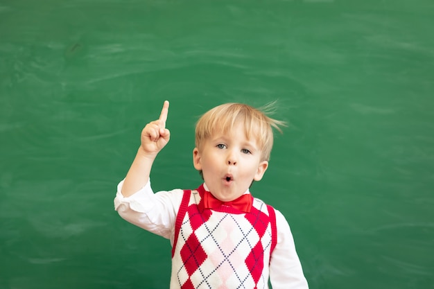 Studente bambino sorpreso che punta il dito contro la lavagna verde.