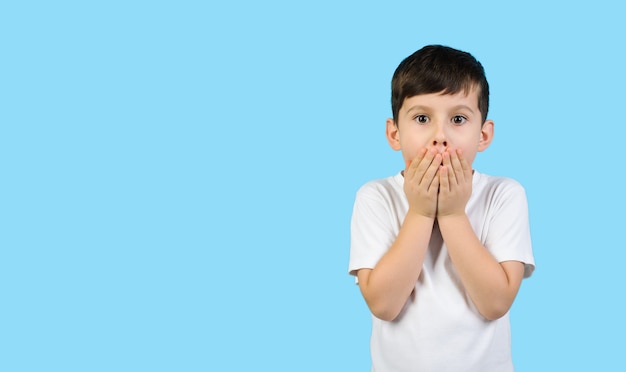 Foto il bambino sorpreso in una maglietta bianca si copre la bocca con le mani