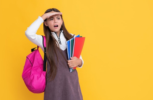 Surprised child with school backpack and workbook on yellow background