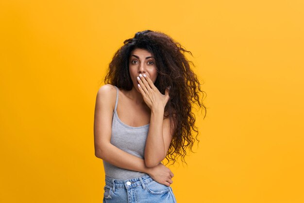 Surprised confused young arab lady covers her mouth with hand\
holding hand on waist isolated on orange background collage\
shocking offer news great sale advertising and app