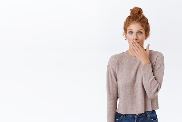 Surprised and curious goodlooking feminine redhead woman with curly hair wear sweater smiling astonished gasping cover mouth and stare camera fascinated raise eyebrows hear shocking news