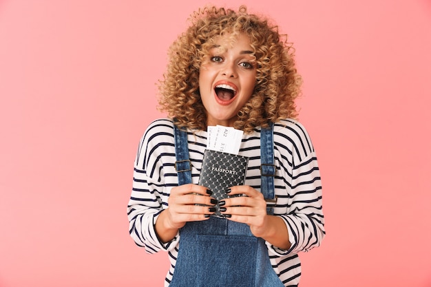 Photo surprised curly woman 20s holding passport and travel tickets while standing