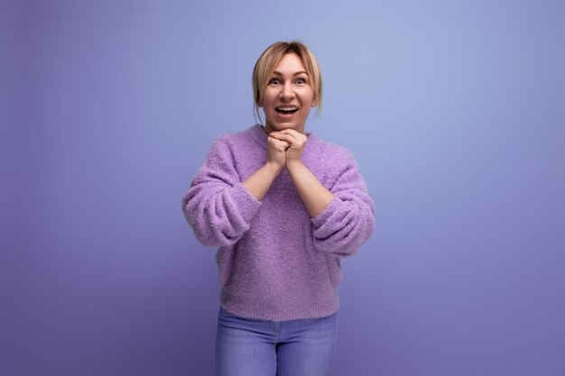 Surprised cute blond woman in lavender sweater on purple background with copy space