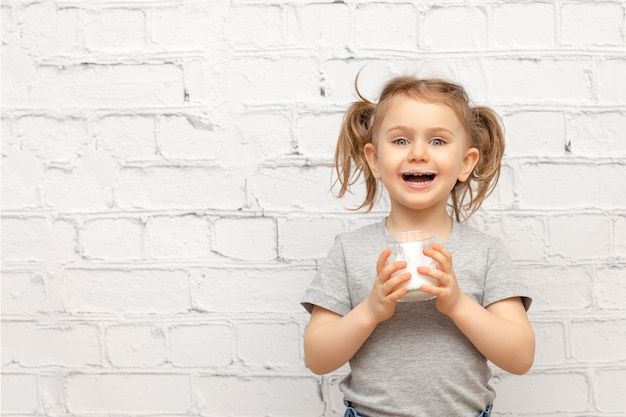 Surprised cute child girl with expression face and mustache of milk on the lips over white brick wall