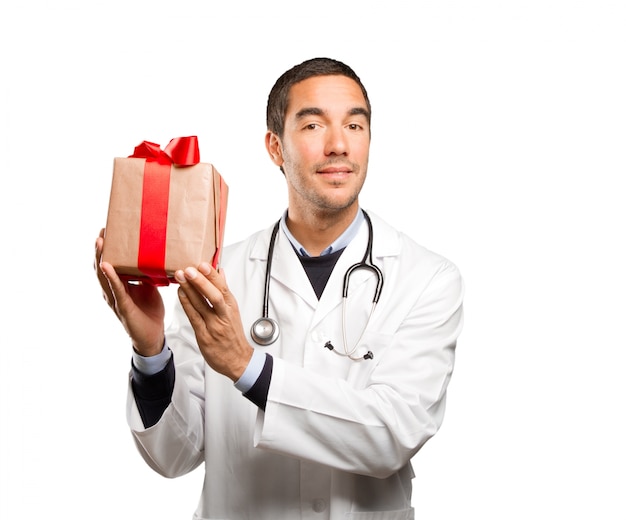 Surprised doctor holding a gift against white background