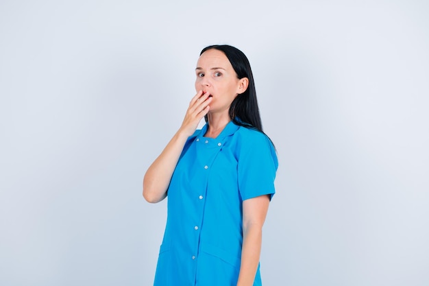 Surprised doctor is looking at camera by holding hand on mouth on white background