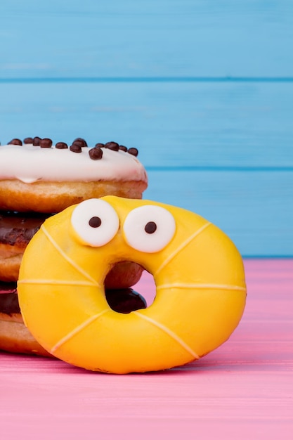 Photo surprised donut on color wooden background. funny donut with shocked emotional expression on colored wood. idea for party.