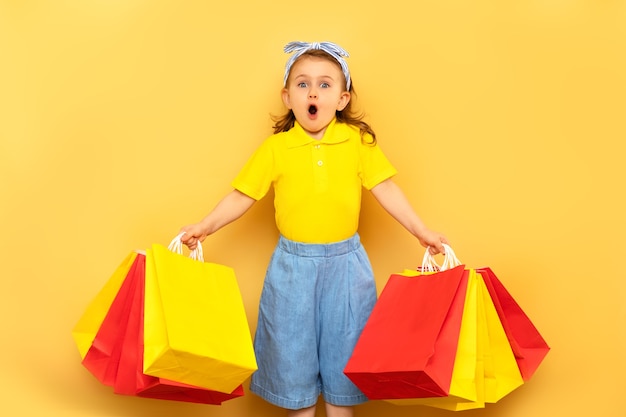 Surprised excited child holding package bags with purchases isolated on yellow wall