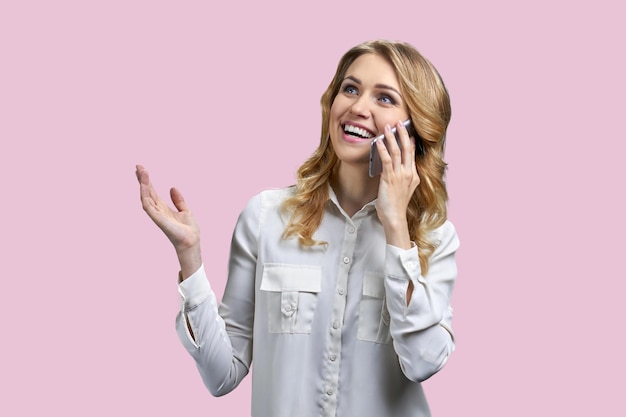 Surprised excited young business woman talking on cell phone against color background