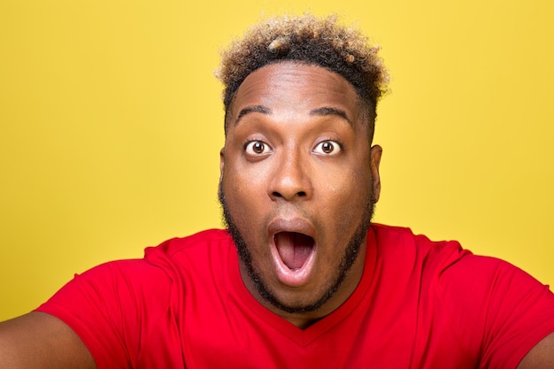 Surprised face of darkskinned curly man close up in frame on yellow background