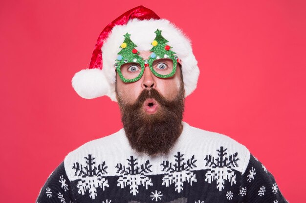 Surprised face. Happy bearded man with santa look. Holiday accessories for santa party. Christmas and New Year celebration. Good mood. Santa is coming. Santa man wear christmas tree party glasses.