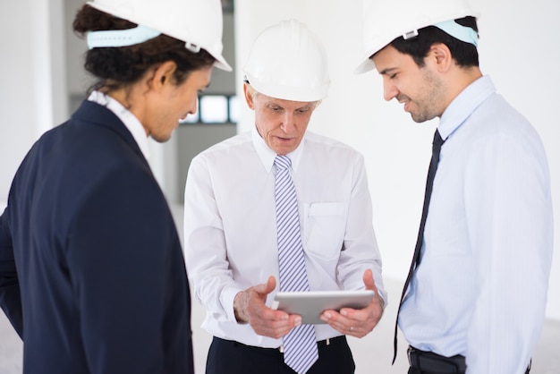 Surprised foreman showing apartment plan on tablet to colleagues