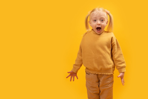 Surprised or frightened girl with her mouth open looks Preschool girl on yellow background Copy space