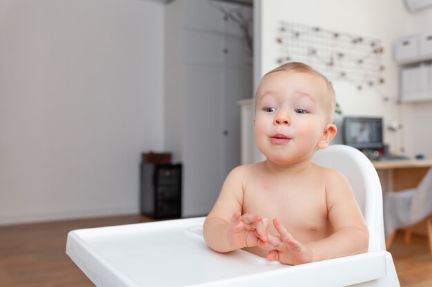 Photo surprised funny beautiful blond baby toddler sitting in chair, apartment background, copy space for text, horizontal