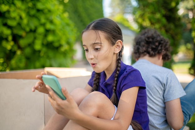 Surprised girl with smartphone and boy back