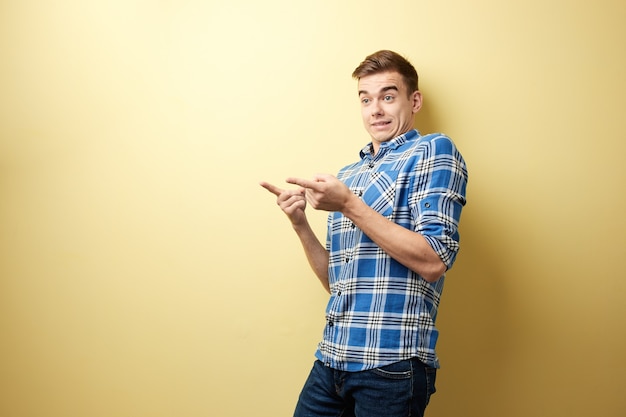 surprised guy stands next to yellow wall in the studio and points with his hands somewhere 