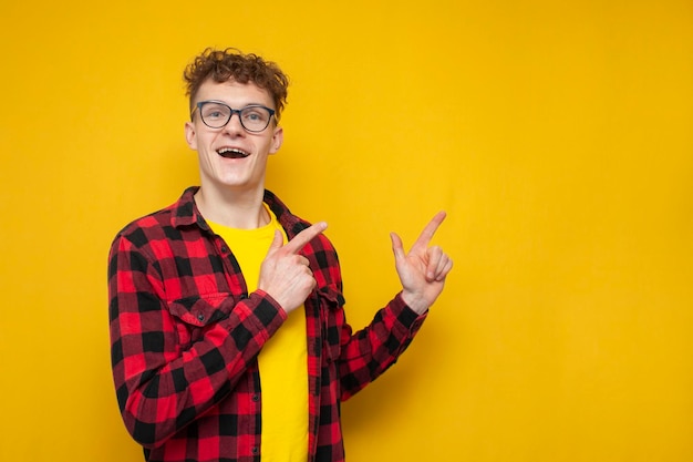 Surprised guy student with curly hair with hands shows space for text nerd advertises copy space