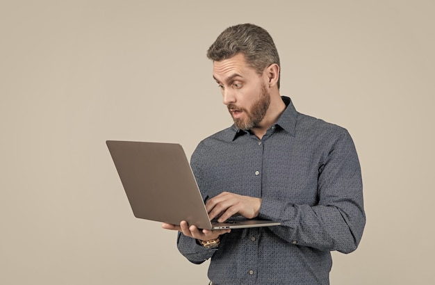 Surprised handsome mature man businessman with beard working online on laptop business