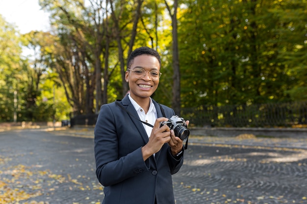 Surprised and happy African American woman looks at the camera and smiles holding a film camera on a walk in the park