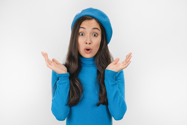 Surprised happy asian woman in blue beret and sweater looking in excitement