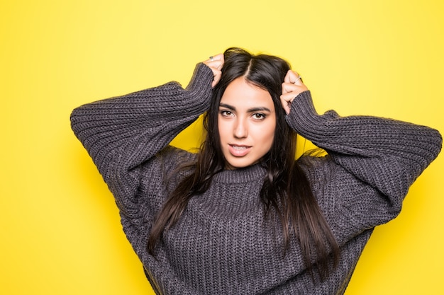 Surprised happy brunette woman in sweater rejoices on yellow