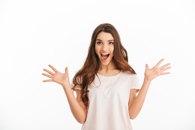 Photo surprised happy brunette woman in t-shirt screaming  over white wall