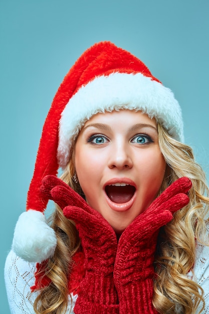 The surprised and happy girl dressed in santa hat. Holiday concept with blue background.
