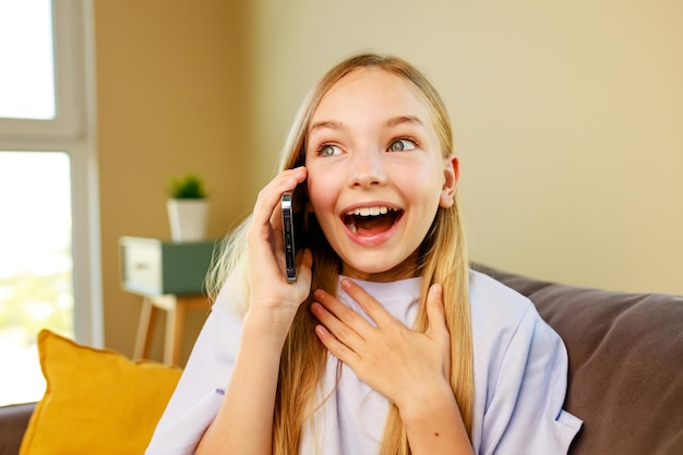 Surprised and happy little girl listen great news by phone in cozy living room at home