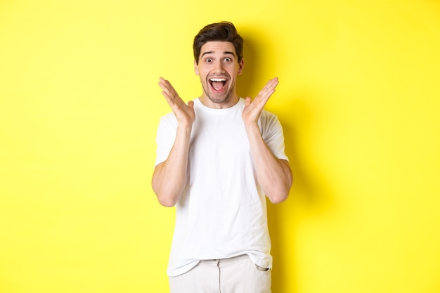 Surprised and happy man reacting to announcement, smiling and looking amazed, standing against yellow wall