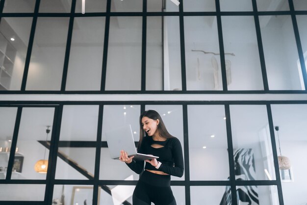 Surprised and happy young woman holding laptop on window background