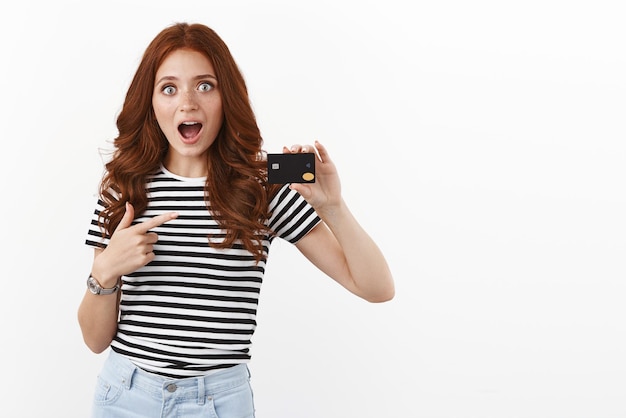 Surprised and impressed speechless cute redhead female student pointing black credit card staring amazed and astonished explain cool banking offers open deposit have big cashback