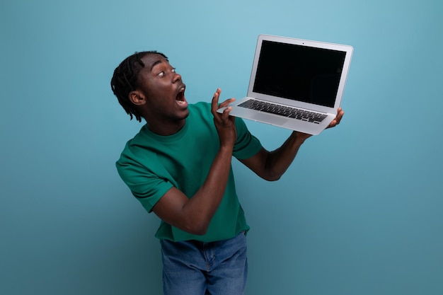 Удивленный радостный африканский молодой брюнет-консультант в повседневной футболке с открытым ноутбуком