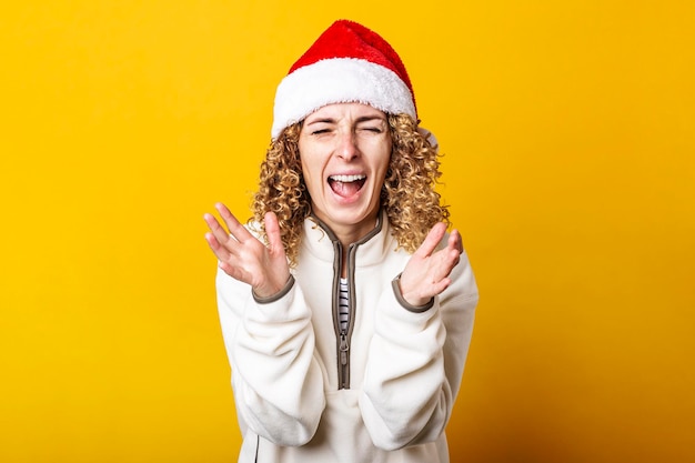 Surprised joyful young woman in santa claus hat on a yellow background.