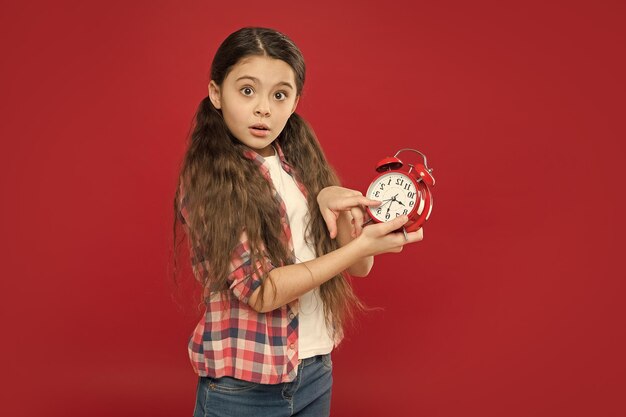 Surprised kid girl showing time on vintage watch alarm