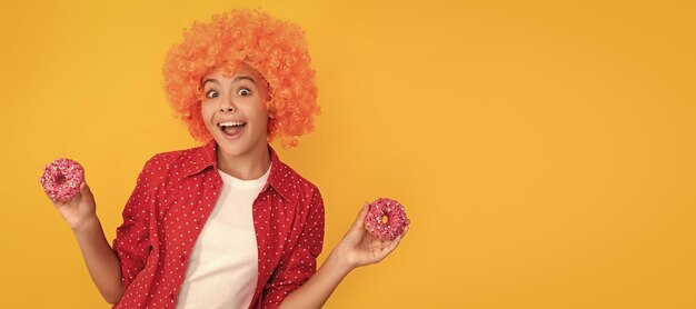 Фото Удивленный ребенок в причудливом оранжевом парике, волосы держат сладкий глазированный пончик, сюрприз подросток со сладостями, плакат, баннер, заголовок, копия пространства