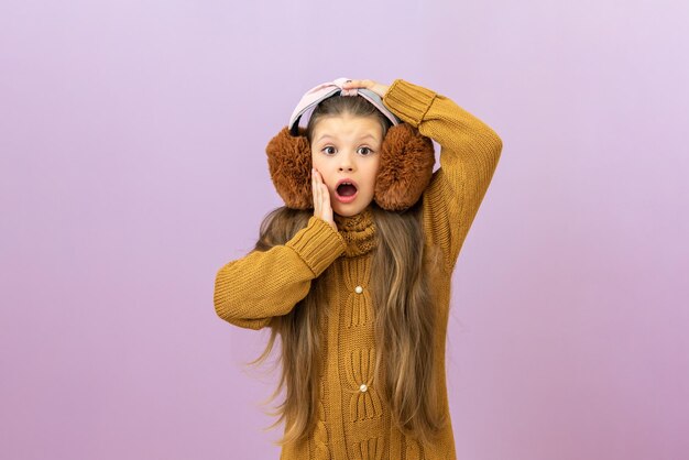 A surprised kid in a winter sweater and warm winter headphones to warm his ears in the cold season a girl on an isolated background