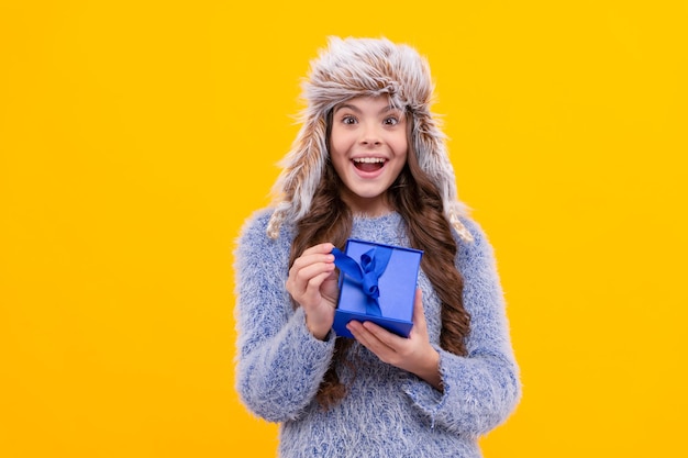 Surprised kid with purchase in hat boxing day teen girl in knitwear on yellow background