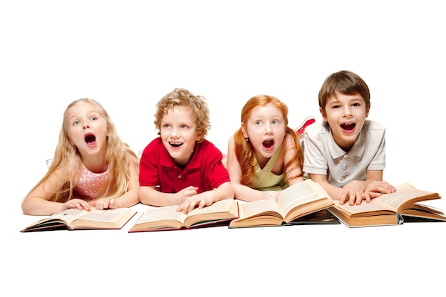 The surprised kids boy and girls laying with books at studio, smiling, laughing, isolated on white. Day of book, education, school, kid, knowledge, childhood, friendship, study children concept