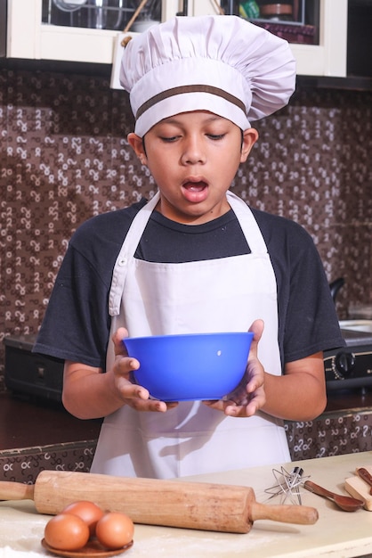 Surprised little chef look at the bowl against kitchen background