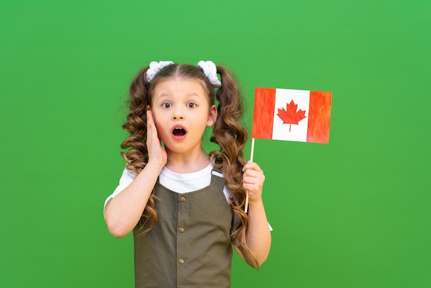 A surprised little girl has a canadian flag on a green isolated background