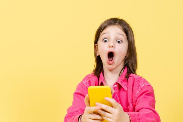 Удивленная маленькая девочка смотрит на телефон и использует социальные сети Родительский контроль над интернет-концепцией