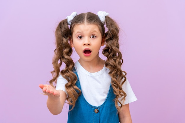 The surprised little girl stretched out her hand forward and asks A child with long curly hair opened her mouth