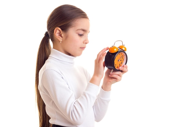 Surprised little girl with long brown ponytail holding a clock on white background in studio