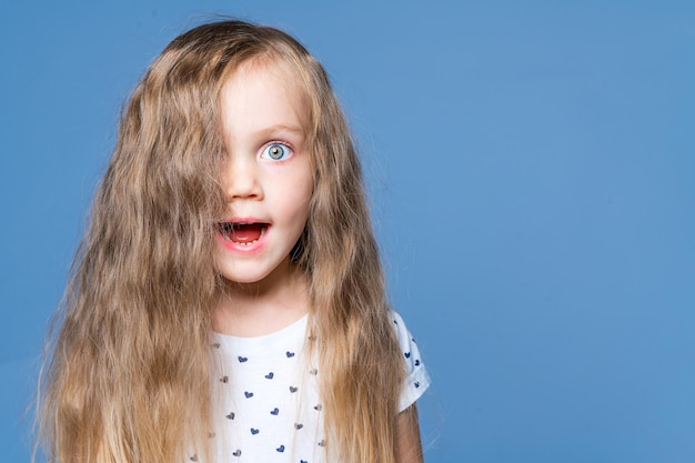 Surprised little girl with open mouth and wide eyes on a blue background in the studio