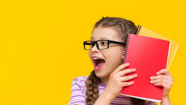 Surprised little schoolgirl on an isolated background a girl with textbooks and notebooks in glasses