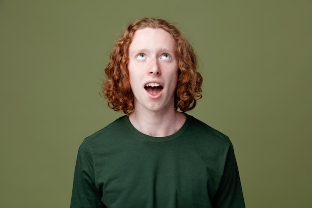 Surprised looking at up young handsome guy wearing green t shirt isolated on green background